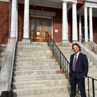 Lawyer wearing suit stands and smiles near entrance of a county court house